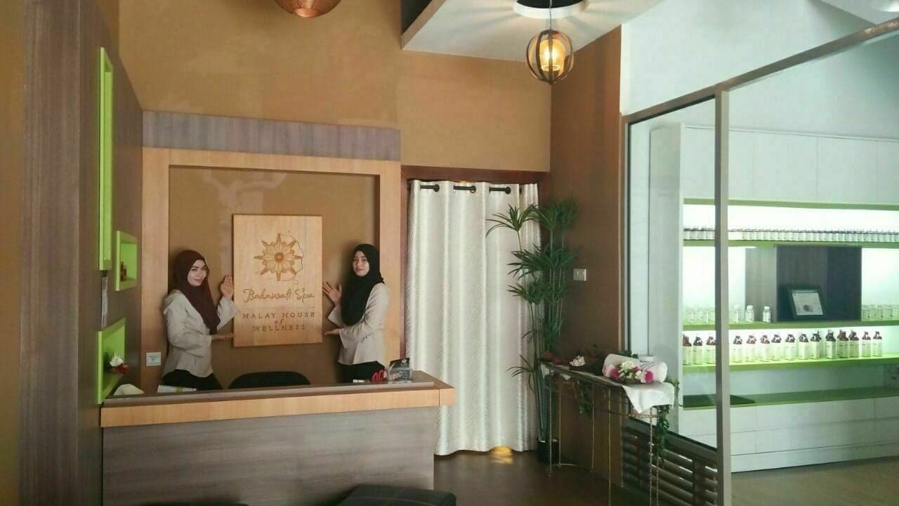 Two Bakawali Spa staff members at the wooden reception desk, beneath a carved Bakawali Spa sign.